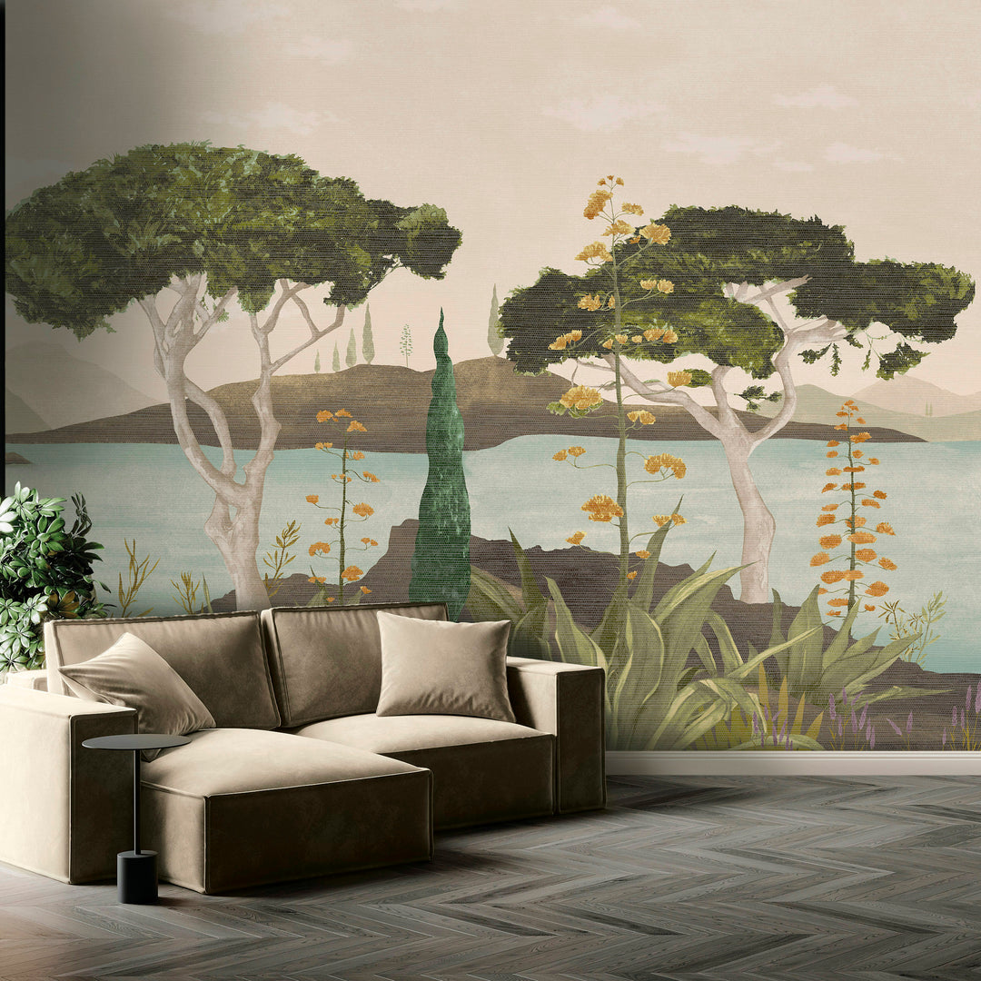 A scenic landscape artwork showing a calm lake or sea with two prominent green trees, distant mountains, and foreground plants in muted beige, green, blue, and orange tones. Scenic Faux Grasscloth Mural - 8294 26 by District Home
