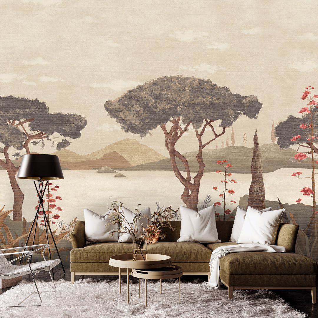 A styled living room featuring a large wall mural with a vintage-style landscape painting of trees, mountains, and water. The room is furnished with a brown sectional sofa, white throw pillows, a black floor lamp, and a white shag rug. Scenic Faux Grasscloth Mural - 8294 45 by District Home