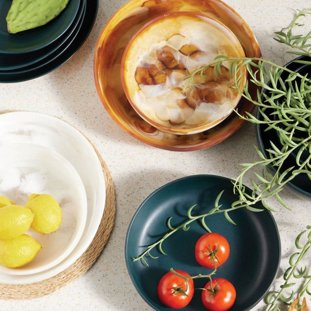 Assorted dishes with food on a light surface, including a bowl of soup, a plate of tomatoes, and a bowl of lemons. District Home